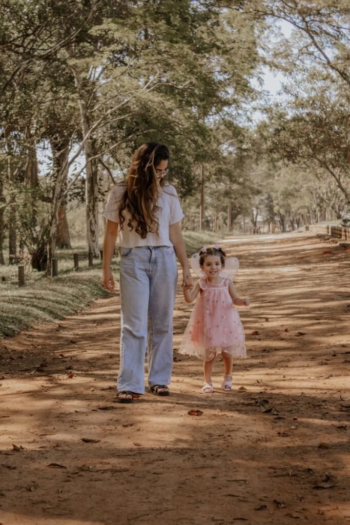 A mother and child hold hands walking down a sunny forest path.