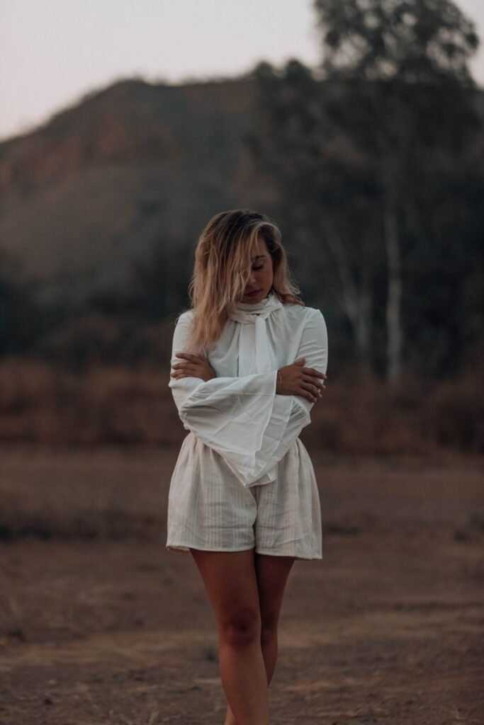A woman stands thoughtfully outdoors in summer, wearing a stylish white dress.