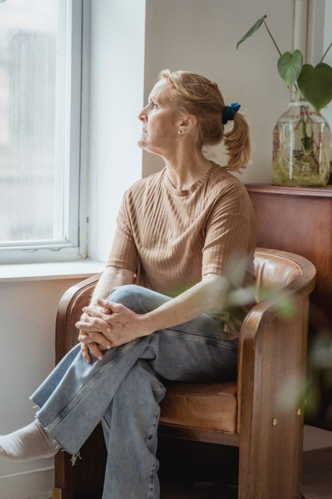 Thoughtful woman gazing outside from an armchair, indoors on a calm day.