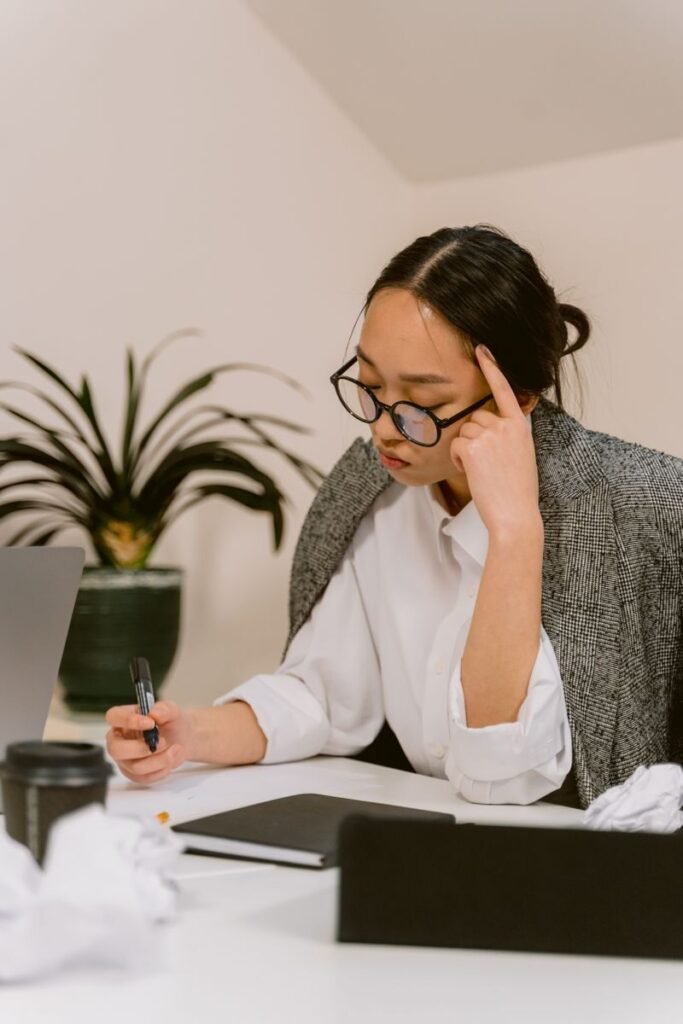 Asian woman in deep thought, working at desk with papers and laptop.