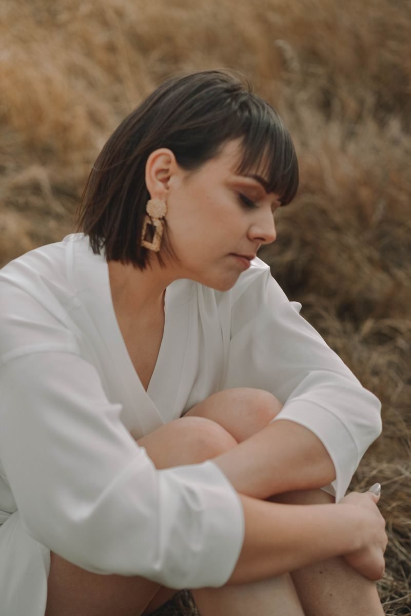 Reflective woman sitting on grass in natural setting, wearing white attire